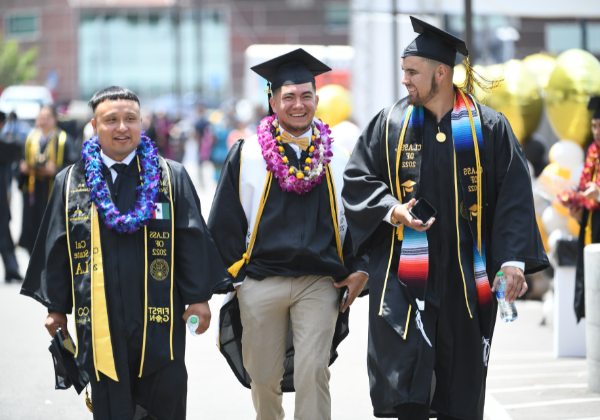 三个男学生戴着毕业礼服走在校园里.